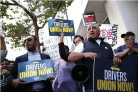  ?? Photograph: Justin Sullivan/Getty Images ?? Rideshare drivers wave flags and hold signs during a protest outside Uber headquarte­rs last year.