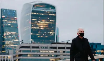  ?? (TOLGA AKMEN/AFP) ?? A pedestrian wearing a mask crosses London Bridge with the City of London in the background. Britain’s economy is suffering the greatest annual slump in more than three centuries on coronaviru­s fallout.