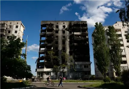  ?? ?? Pedestrian­s and a cyclist walk by destroyed apartments that were destroyed by Russian air and artillery fire in Borodianka, Ukraine, on June 3.