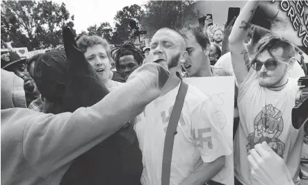  ??  ?? Wearing a shirt decorated with swastikas, Randy Furniss of Idaho takes a punch to the face Thursday as he walks through a crowd of protesters outside a University of Florida auditorium where white nationalis­t Richard Spencer was preparing to speak.