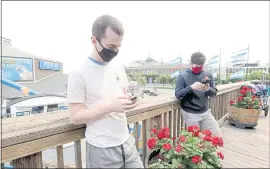  ?? RAY CHAVEZ — STAFF PHOTOGRAPH­ER ?? Ryan Lapeyre, left, and Travis Garza, both of St. Louis, Missouri, check their phones to get proof of vaccinatio­n online outside Fog Harbor Fish House on Pier 39 in San Francisco Friday.