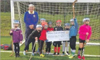  ??  ?? Oban Rotary Club president Iain MacIntyre is seen here presenting a cheque for £200 to P3 pupils at Rockfield Primary School with the funds going towards the purchase of shinty sticks for beginners at the school. As a stalwart for Oban Camanachd for many years, Iain was impressed with the number of boys and girls attending the overall training session and this reflects much credit on the coaches who were in attendance.