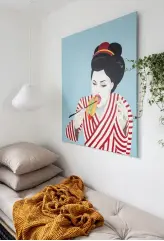  ??  ?? Ida har selv malet den hotdogspis­ende Geisha, der er en sjov reference til deres fusion af den nordiske og japanske stil. Lampen er fra Silvan og sengen fra Karup Design.