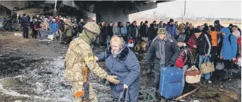  ?? ?? A Ukrainian serviceman helps evacuees gathered under a destroyed bridge, as they flee the city of Irpin, northwest of Kyiv (Photo by DIMITAR DILKOFF/AFP via Getty Images)