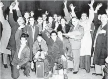  ?? GEORGE QUINN/CHICAGO TRIBUNE ?? A group of displaced people from Greece hold up their arms at Union Station in Chicago on March 23, 1951, after arriving from the east. At right, with portfolio, is George Rendas, chairman of a Chicago displaced persons committee.