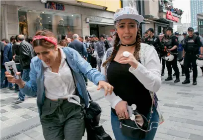  ?? AFP ?? Two women walk away as Turkish riot police clash with protesters at Taksim Square on Monday. —