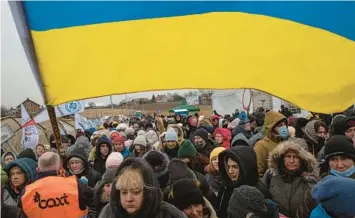  ?? VISAR KRYEZIU/AP 2022 ?? Volunteer Oleksandr Osetynskyi holds a Ukrainian flag as he directs refugees March 7 in Medyka, Poland.