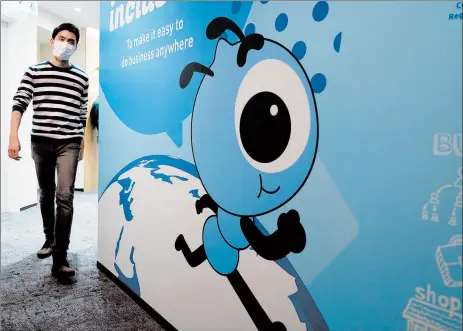  ?? KIN CHEUNG/AP ?? An Ant Group employee walks by a graphic of the financial technology company’s mascot Friday in Hong Kong. Ant Group operates Alipay, a dominant digital wallet in China.