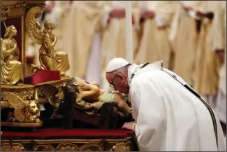  ?? The Associated Press ?? CHRISTMAS EVE MASS: Pope Francis kisses a statue of Baby Jesus as he celebrates the Christmas Eve Mass on Sunday in St. Peter’s Basilica at the Vatican.