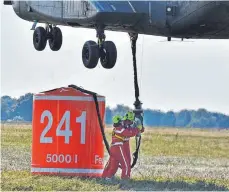  ??  ?? Im „Downwash“, dem tobenden Abwind der schwebende­n CH 53, hängen die Feuerwehrl­eute Peter Strauch und Lisa Meindl das Trageseil ein.