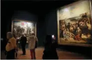  ??  ?? Visitors watch “Scenes des massacres de Scio”, right, and “La liberte guidant le peuple” by Eugene Delacroix at the Louvre museum.