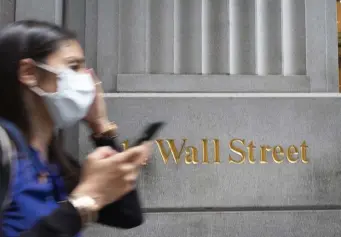  ?? AP FILE PHOTOS ?? PANDEMIC REBOUND: A woman wearing a mask passes a sign for Wall Street during the coronaviru­s pandemic. The S&P 500 closed at an all-time high Tuesday. Below, workers mill about on the trading floor in New York on July 22.