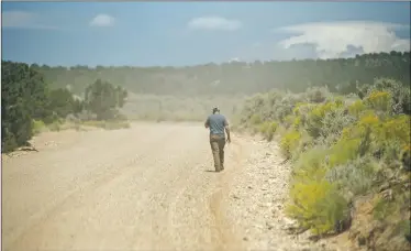  ?? Morgan Timms ?? A local man walks through a cloud of dust left by cars Friday (Aug. 24) near Amalia, a tiny community that was largely unknown outside of the area before a raid on a compound on a nearby road.