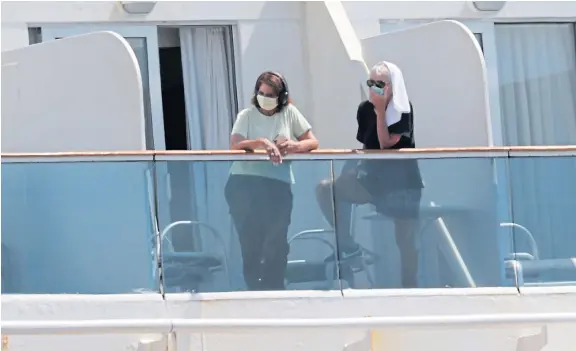  ?? Picture: AP. ?? Passengers wearing protective masks look out from their balcony on the Coral Princess cruise ship while docked at Miami.