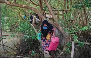  ?? ?? Asiyah walks on a narrow concrete slab, the only way to access her abandoned house, while carrying plastic bags containing items she recovered from the house in Mondoliko.