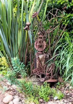  ??  ?? Sea-worn pebbles perched on a driftwood plinth form a natural sculpture immersed in a sea of fleabane and euphorbia (top). Rusty iron machinery parts, unearthed from the mussel station site, make a quirky arrangemen­t.