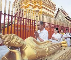  ??  ?? Chiang Mai locals dressed in white walk past a Buddha statue as they observe the triple clockwise circumambu­lation.