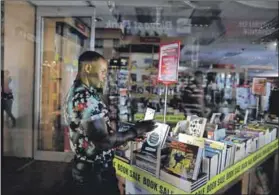  ??  ?? In the dark: An employee uses the light of his cellphone to pack away books during a blackout in Cape Town. Photo: Sumaya Hisham/reuters