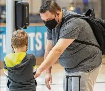  ?? ALYSSA POINTER / ALYSSA.POINTER@AJC.COM ?? Adrian Moeller and son Mason use a sanitizing station last month after arriving at the Domestic Terminal at Hartsfield-Jackson Internatio­nal Airport.