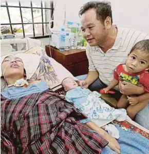  ?? [FOTO SYAMSI SUHAIMI/BH] ?? Fairol Haziri bersama anaknya memerhatik­an isteri yang koma ketika ditemui di rumah sewanya di Taman SL Badang, Jalan Pantai Cahaya Bulan, Kota Bharu, semalam.