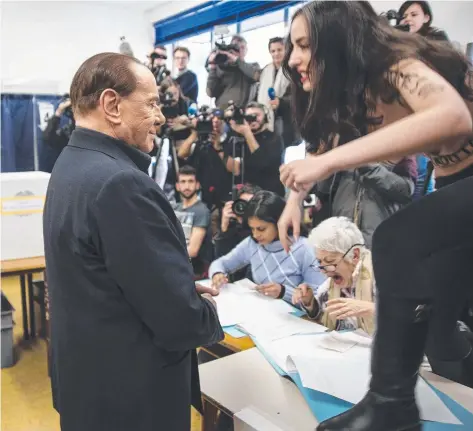  ??  ?? BALLOT BLUNDERS: A protester confronts Silvio Berlusconi as he prepares to vote in the Italian elections. Across her chest are words which translate to: “Berlusconi, you have expired”. Below, some seemed reluctant to go into the booths in Florence.