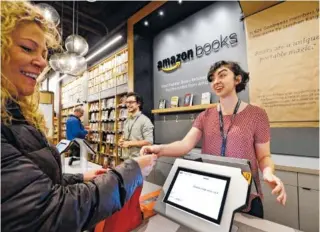  ?? AP PHOTO/ELAINE THOMPSON, FILE ?? Customer Kirsty Carey, left, gets ready to swipe her credit card for clerk Marissa Pacchiarot­ti, as she makes one of the first purchases at the opening day for Amazon Books in Seattle. Amazon has opened more than a dozen locations of Amazon Books,...