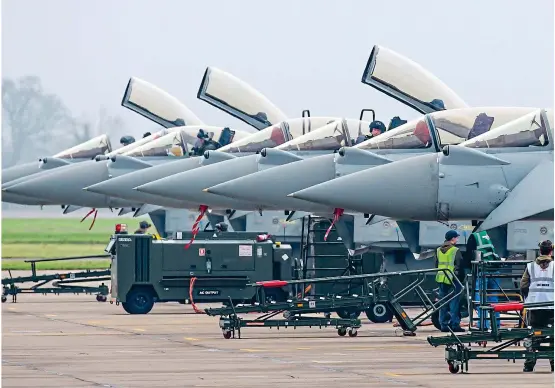  ??  ?? Firepower: Typhoons are prepared for flight at RAF Coningsby in Lincolnshi­re yesterday. Right: A pilot waves from the cockpit