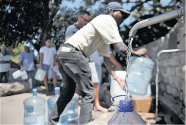  ??  ?? Capetonian­s stand in a queue to collect natural spring water from the Brewery Spring in Newlands.