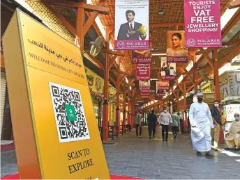  ?? Virendra Saklani/Gulf News ?? ■ Visitors walk past the City of Gold Explore Map QR Code kiosk at gold souk.