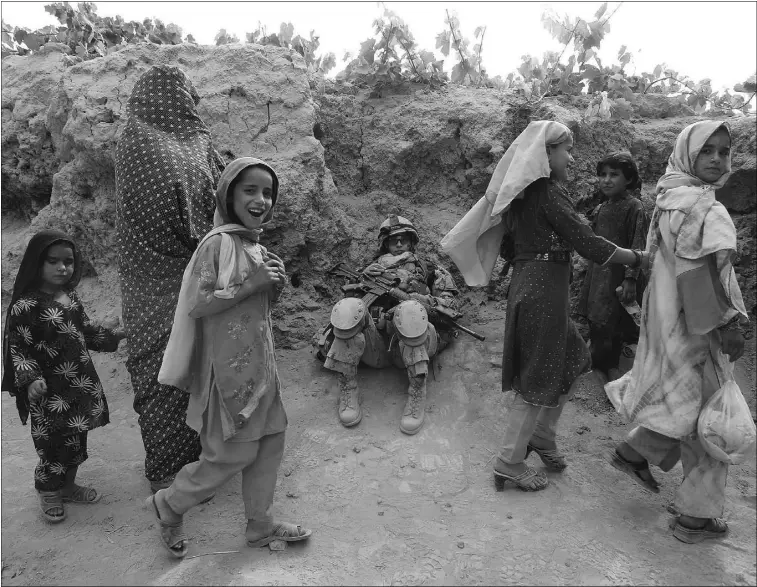  ?? Baz Ratner
, Reuters, FILE ?? Afghan girls walk past a female Canadian soldier as she rests during a patrol in Kandahar province last June. Widespread traditions of honour-killing date back to the pre-islamic era.