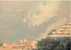  ??  ?? A helicopter swoops down to make a water drop over a wildfire at Estepona, Spain.