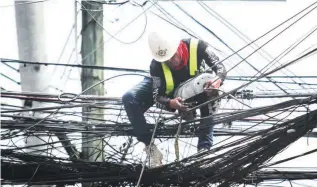  ??  ?? ORDER IN ALL THE CHAOS – A worker tries to fix a lashing machine that will bunch together telecommun­ication cables in downtown Davao City. (Keith Bacongco)