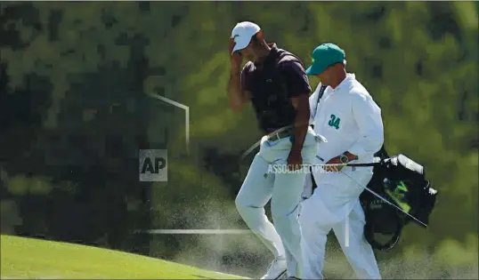  ?? ASSOCIATED PRESS ?? Tiger Woods and caddie Lance Bennett shield, their faces from the blowing sand on the 18th hole during second round at the Masters golf tournament at Augusta National Golf Club Friday, April 12, 2024, in Augusta, Ga.