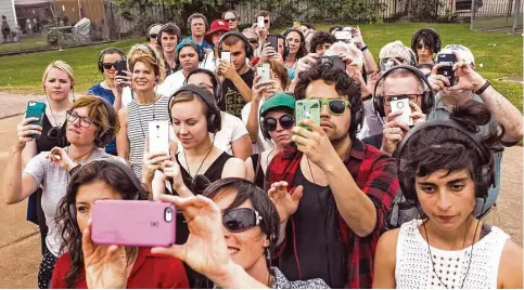  ??  ?? Participan­ts of “Remote Houston” stop and take a group photo from a mirror reflection at Eastwood Park during their audio-guided tour.