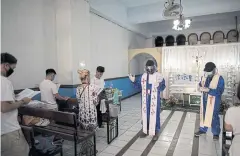  ??  ?? Father Eduardo and Father Rey say prayers during a wake where attendees wear face masks in a funeral chapel in Caloocan.