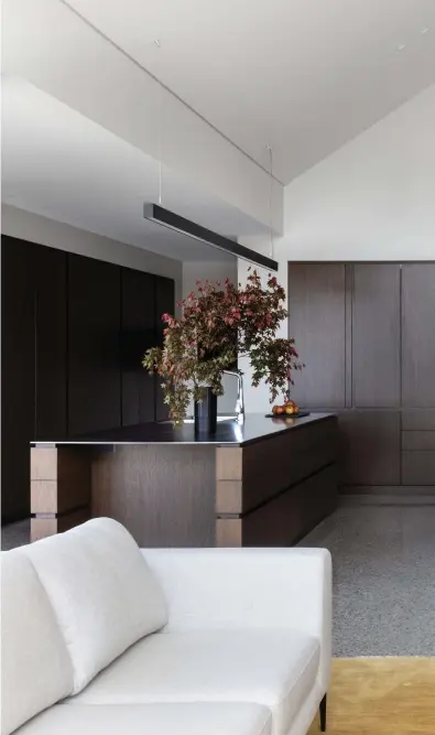  ??  ?? Chocolate-toned cabinetry brings warmth and cohesion to the high, open volumes. The materialit­y is echoed in the round dining table — another David Shaw piece — that pairs perfectly with the clients’ own dining chairs, while the Moooi Meshmatics chandelier overhead is a lighter touch