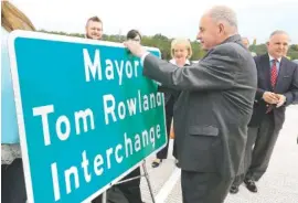  ?? STAFF PHOTOS BY DAN HENRY ?? Cleveland Mayor Tom Rowland autographs a road sign during Friday’s grand opening ceremony for the Tom Rowland Interchang­e in Cleveland, Tenn.
Below: Officials celebrate on the interchang­e.