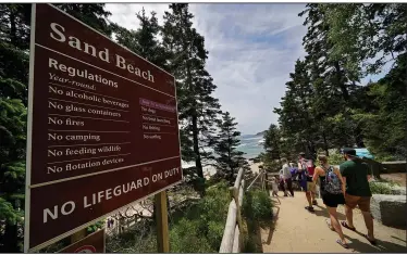  ?? (AP/Robert F. Bukaty) ?? Beachgoers walk by a sign that warns of the absence of lifeguards June 11 at Sand Beach in Acadia National Park.