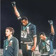  ??  ?? Tommie Smith, center, and John Carlos extend gloved hands in racial protest at the 1968 Olympics. AP