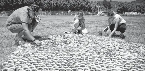  ?? REUTERS ?? Artist Aida Sehovic (centre) helps install her collection of some 8,000 traditiona­l ceramic cups filled with Bosnian coffee at the Potocari-srebrenica Memorial Centre for victims of the 1995 massacre of Muslim men and boys by Serb forces, in eastern Bosnia.