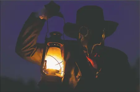  ??  ?? James Gregory, co-owner of Terror Town, holds a lantern as he wears a black plague mask while scaring visitors. (AP/Aaron Doster)