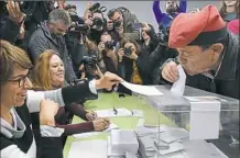  ?? Lluis GeneAFP/Getty Images ?? A man wearing an Catalan barretina hat kisses his ballot before casting his vote Thursday for the Catalan regional election at a polling station in Barcelona.