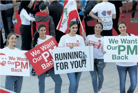  ?? HASSAN AMMAR/THE ASSOCIATED PRESS ?? Lebanese women hold placards supporting the outgoing Lebanese Prime Minister Saad Hariri to return from Saudi Arabia during the Beirut Marathon in Beirut, Lebanon, on Sunday.