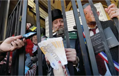  ?? —AFP ?? PARIS: Transactio­ns and Citizen’s Action (ATTAC) dressed as prisoners and mocking characters (behind bars, from left) Ronald McDonald, a banker and President of the European Commission Jean-Claude Juncker as they stand in the premises of a BNP bank...