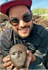  ?? COURTESY DREW MICHAEL ?? Artist Drew Michael holds a mask, excavated just moments before, at the Nunalleq archaeolog­ical site, August 2017