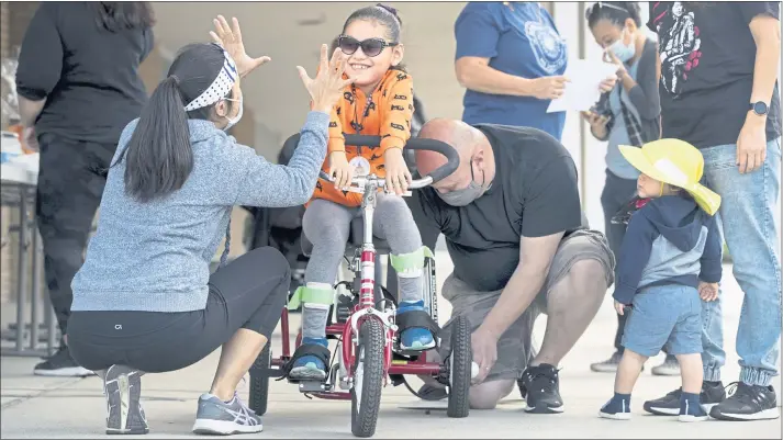  ?? KARL MONDON — STAFF PHOTOGRAPH­ER ?? Coraline Carrasco, 8, of Gilroy, is outfitted with a tricycle by her father, Eddie Carrasco, and Bay Area Trykers volunteer Katrina Ng during a Tryke-a-Thon fundraiser in San Jose.