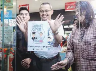  ??  ?? Dzulkifli (centre) places the MACC Careline sticker on the glass door of a 7-Eleven outlet as Zurainah (right) looks on during the launch of the ‘Sahabat SPRM careline’ at Berjaya Times Square yesterday.
