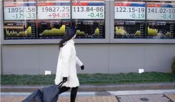  ?? — Reuters ?? A woman walks past electronic boards showing stock prices and Japanese Yen’s exchange rate outside a brokerage at a business district in Tokyo.