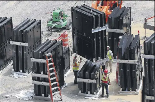  ??  ?? Workers assemble and hoist panels by crane that form the giant halo board around the retractabl­e roof. Work also continues on the roof itself, which consists of eight movable steel panels, called petals, each weighing 500 tons.