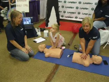  ?? Staff photo by Greg Bischof ?? ■ LifeNet Employee Tina Bell, far left, watches as her daughter, Emily Bell, attempts to learn CPR on Saturday during the 23rd annual Wild About Wellness Children’s Health Fair at the Four States Fairground­s Entertainm­ent Center. LifeNet employees Netra Dutton and Shomeka Thomas, far right, also participat­e.